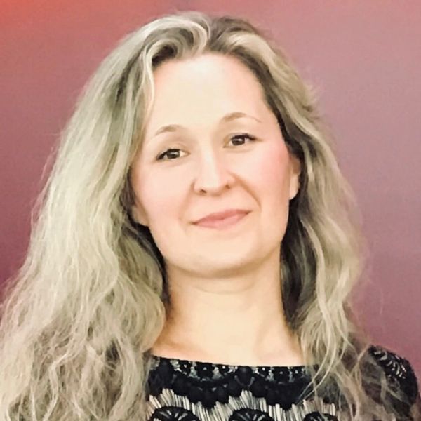 Smiling woman with long, wavy blonde hair against a soft purple background, conveying a warm and approachable demeanor.