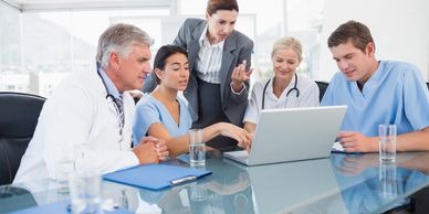 Medical team collaborating around a laptop, discussing patient data and strategies in a bright, modern conference room.