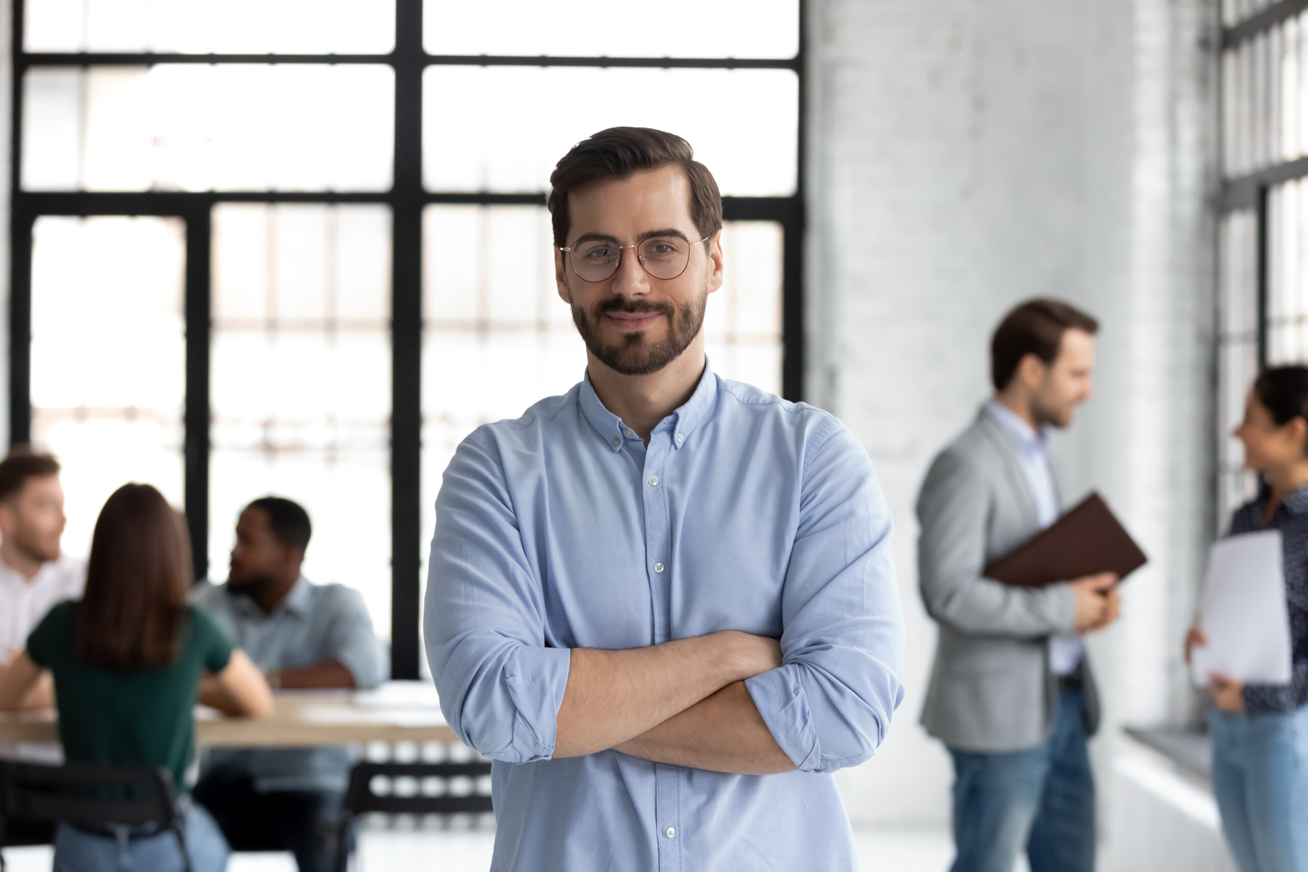 Head shot portrait smiling confident businessman wearing glasses standing in modern office room with arms crossed, diverse colleagues on background, executive boss startup founder looking at camera; Shutterstock ID 1792769593; purchase_order: Limited 5/13; job: ; client: ; other:
